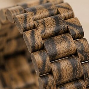 May include: A watch band constructed from individual wooden links featuring a natural brown and black grain pattern. The band is composed of rectangular segments connected in a flexible chain design, showcasing the organic texture of the wood.