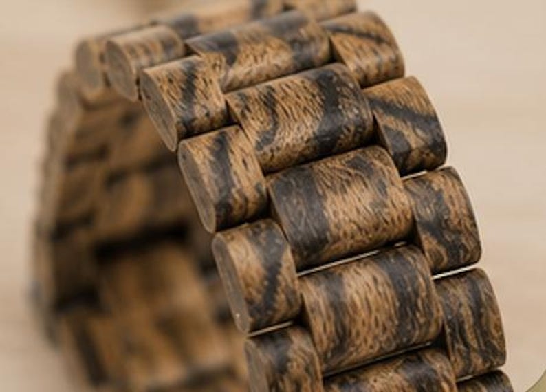 May include: A watch band constructed from individual wooden links featuring a natural brown and black grain pattern. The band is composed of rectangular segments connected in a flexible chain design, showcasing the organic texture of the wood.