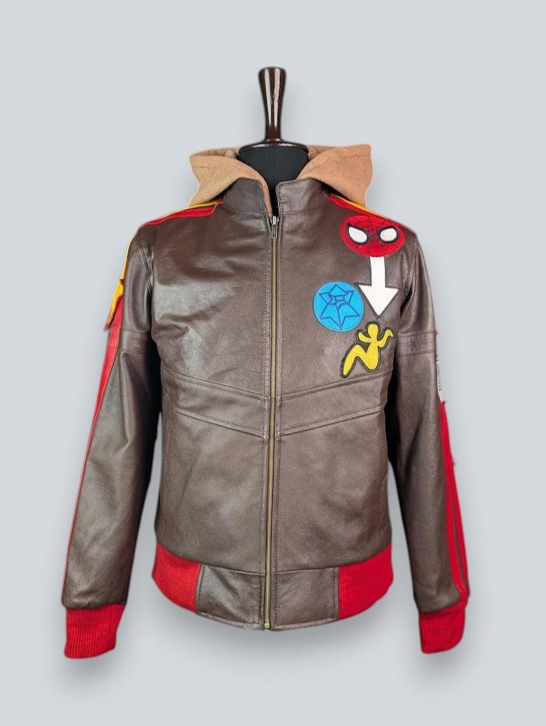 May include: A brown leather jacket featuring a tan hood, a full-length front zipper, and red ribbed cuffs and hem. The chest is decorated with colorful embroidered patches, including a red spider mask, a blue star, and a yellow figure.
