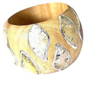 May include: A wide, rounded wooden bangle bracelet featuring inlaid, leaf-shaped segments of iridescent, cracked shell material. Each shell inlay is outlined with a thin, silver-toned metallic border, contrasting against the light brown wood grain.