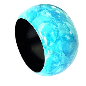 May include: A wide bangle bracelet featuring a vibrant turquoise and sky blue marbled pattern on the exterior surface. The interior of the circular accessory is finished in a solid matte black, providing a stark contrast to the bright blue tones.