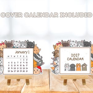 May include: A 2027 desk calendar set featuring a border of illustrated cats in various colors and expressions. One card displays the month of January 2027, while the other shows the text 2027 CALENDAR with four cat paws. Both rest on wooden easels.