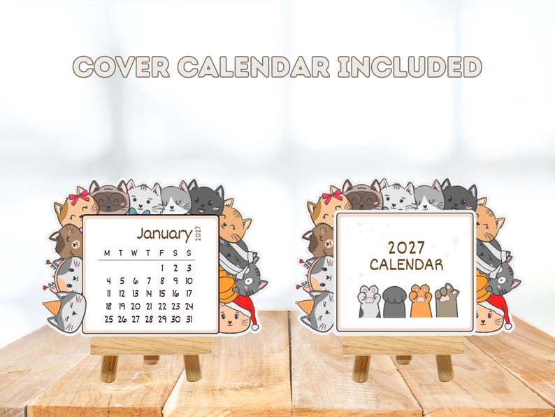 May include: A 2027 desk calendar set featuring a border of illustrated cats in various colors and expressions. One card displays the month of January 2027, while the other shows the text 2027 CALENDAR with four cat paws. Both rest on wooden easels.