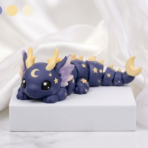 May include: A dark blue articulated dragon figurine featuring light yellow crescent moon and star patterns on its body. The dragon has large black eyes, light purple side fins, and a yellow crescent moon shape at the tip of its segmented tail.