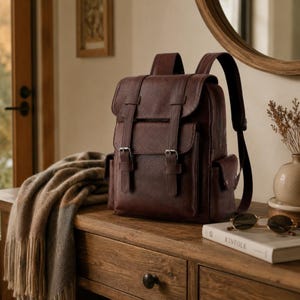 Peut inclure: Un sac à dos marron foncé doté d'un rabat avec deux sangles verticales, de boucles métalliques argentées et de poches latérales. Le sac possède des bretelles réglables et une forme rectangulaire structurée avec une finition texturée sur l'extérieur.