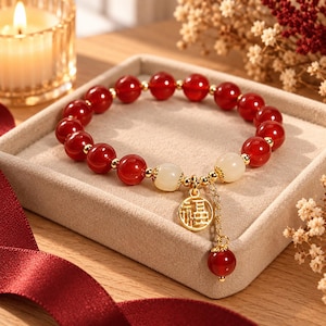 May include: A beaded bracelet featuring polished red agate beads and two smooth white jade beads. The bracelet includes small gold-toned metal spacers and a gold-toned circular charm with the Chinese character Fu, plus a dangling red bead.
