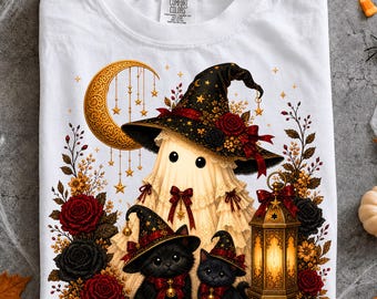 Puede incluir: Una camiseta blanca con un gráfico de un fantasma que lleva un gran sombrero de bruja negro adornado con rosas rojas y estrellas doradas. Dos gatitos negros con sombreros a juego se sientan junto a una linterna brillante, una luna y rosas.