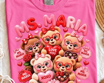 May include: A bright pink t-shirt featuring a graphic of four brown teddy bears wearing heart-shaped glasses and bows. The bears hold red heart-shaped boxes of chocolates and hearts with the text MS. MARIA, LOVE YOU, and XOXO.