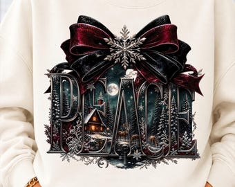 May include: A cream-colored sweatshirt featuring a large graphic print of the word PEACE. The letters contain a winter forest scene with a cabin, deer, and a full moon. A large dark red and black bow with a silver snowflake sits on top.