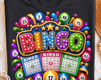 May include: A black t-shirt featuring a colorful graphic of the word BINGO in illuminated marquee-style letters. The design includes three bingo cards, various numbered bingo balls, gold stars, and vibrant abstract splashes of color.
