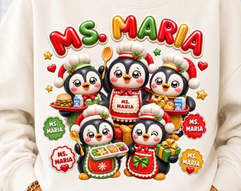 May include: A cream-colored sweatshirt featuring a graphic of five cartoon penguins wearing chef hats and aprons. The text "MS. MARIA" appears at the top and in several decorative bubbles. The penguins hold items like food trays, milk cartons, and a gift.
