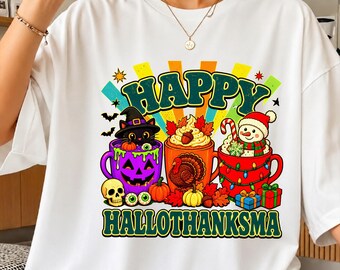 Puede incluir: Una camiseta blanca con un gráfico colorido y el texto HAPPY HALLOTHANKSMA. El diseño incluye tres tazas: una taza morada de calabaza con un gato negro, una taza naranja con un pavo y una taza roja con un muñeco de nieve y regalos.