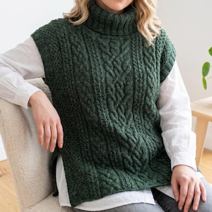 May include: A dark forest green sleeveless sweater vest featuring a chunky turtleneck collar and a prominent vertical cable knit pattern. The garment has wide armholes, a ribbed hem, and side slits, layered over a crisp white long-sleeve shirt.