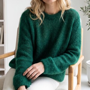 Può includere: Un maglione a maniche lunghe con girocollo in un colore verde bosco intenso. Il capo presenta una trama lavorata a maglia testurizzata e leggermente soffice con dettagli a coste sui polsini e sullo scollo, offrendo un aspetto solido e uniforme.