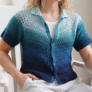 May include: A short-sleeved crochet button-down shirt featuring an ombre color gradient that transitions from light blue at the collar and shoulders to a deep navy blue at the hem. The shirt has a classic collar, dark buttons, and a textured pattern.
