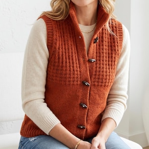 May include: A burnt orange knit waistcoat featuring a high collar, a textured ribbed pattern on the upper section, and a smooth knit lower section. The waistcoat is fastened with five dark brown toggle buttons down the front and is layered over a cream jumper.