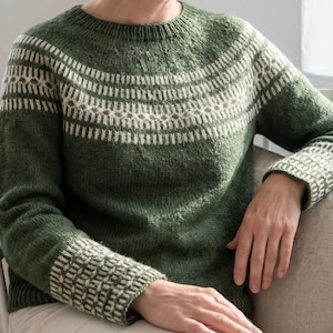 May include: A long-sleeved knit jumper in a deep forest green colour featuring a round neckline and a contrasting cream-coloured geometric pattern around the yoke and the cuffs. The garment is constructed with a ribbed collar and ribbed sleeve hems.