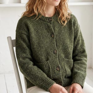 May include: A long-sleeve, crew-neck cardigan in a textured olive green knit fabric. The garment features a front button closure with five dark brown buttons, ribbed cuffs, a ribbed hem, and two front patch pockets integrated into the knit design.