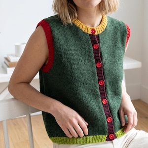 May include: A sleeveless knit vest in dark green featuring a mustard yellow ribbed crew neckline, red ribbed armholes, and a lime green ribbed hem. The front placket is dark purple with seven bright red buttons running down the center.