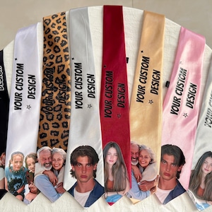 Puede incluir: Una colección de ocho corbatas de satén en varios colores, incluyendo negro, blanco, estampado de leopardo, plata, rojo, oro, rosa y gris claro. Cada corbata presenta el texto impreso "YOUR CUSTOM DESIGN" y un retrato fotográfico único.