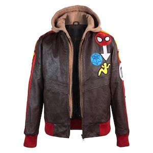 Può includere: Una giacca in pelle marrone scuro con inserto a cappuccio beige, polsini e orlo a coste rossi e strisce laterali gialle e rosse. Il petto è decorato con toppe colorate, tra cui una maschera di Spider-Man, una ragnatela blu e una sagoma gialla.