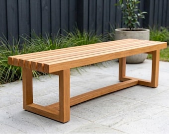 Op de afbeelding: Een rechthoekige houten bank met een zitting van latten met gelijkmatig verdeelde horizontale planken. De bank is geconstrueerd met vier stevige poten die aan de basis verbonden zijn door een horizontale steunbalk, met een natuurlijke houtnerf.