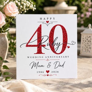 May include: A square white greeting card featuring the text HAPPY 40 Ruby WEDDING ANNIVERSARY Mum & Dad 1986 2026. The number 40 is printed in a large red glitter texture. The design includes small red heart icons and black decorative flourishes.