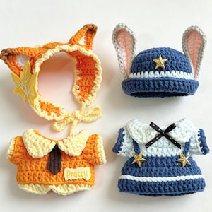 Pode incluir: Dois gorros e duas camisas de crochê para bonecas pequenas. Um gorro é laranja com orelhas de raposa e uma folha amarela, o outro é azul com orelhas de coelho e uma estrela dourada. Uma camisa é laranja com gola e a palavra Pretty, a outra é azul e branca.