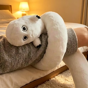 May include: A white plush toy shaped like a long, coiled creature with a rounded head, large black and white eyes, and small limbs with black-tipped claws. The soft, fuzzy material wraps around a gray sleeve, creating a coiled, flexible form.