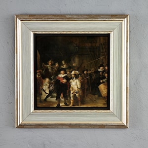 Könnte beinhalten: Eine gerahmte Reproduktion von Rembrandts Nachtwache, die eine Gruppe von Figuren in Kleidung des 17. Jahrhunderts zeigt. Das Kunstwerk ist in einen breiten, hellen Holzrahmen mit strukturierter Oberfläche und dezentem Metallglanz gefasst.