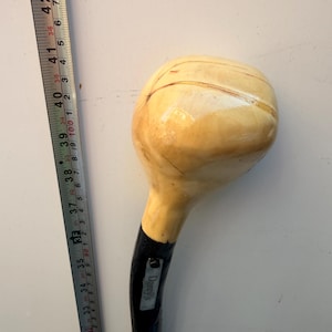 May include: A wooden walking stick with a large, rounded, light-colored top and a black shaft. A metal plate with the text 'Darey's' is attached to the shaft. A metal measuring tape is positioned alongside, showing the stick is over 40 inches long.