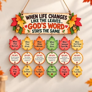 May include: A wooden wall hanging featuring the text "WHEN LIFE CHANGES LIKE THE LEAVES... GOD'S WORD STAYS THE SAME" decorated with autumn leaves and acorns. Six vertical strands of wooden leaf and circle shapes display inspirational messages.