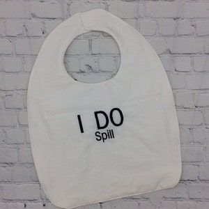 Puede incluir: Babero blanco con abertura para el cuello y el texto "I DO Spill" en negro. El babero está hecho de un material suave y absorbente, diseñado para atrapar derrames y proteger la ropa durante la hora de comer. Accesorio práctico.