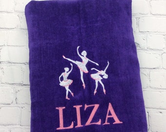 Könnte beinhalten: Tiefviolettes Handtuch mit drei Balletttänzerinnen in weißen Tutus und rosa Schuhen bestickt. Der Name "LIZA" ist in Rosa unter den Tänzerinnen gestickt. Das Handtuch wird vor einer weißen Backsteinmauer präsentiert.
