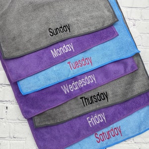 May include: A set of microfiber cleaning cloths in shades of grey, blue and purple, each embroidered with a day of the week: Sunday, Monday, Tuesday, Wednesday, Thursday, Friday, and Saturday. Ideal for cleaning.