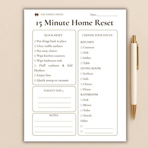 Op de afbeelding: Een witte 15 Minute Home Reset checklist bedrukt met donkerbruine tekst en randen, met secties voor Quick Reset, Today's Top 3, Notes en Choose Your Focus voor keuken, woonkamer en badkamer, vergezeld van een gouden pen.