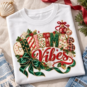May include: A white t-shirt featuring a festive graphic with the text "CHRISTMAS Vibes" in a variety of quilted and plaid patterns. The design includes a large green satin bow, holly leaves, red berries, and hanging ornaments in red and gold.