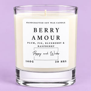 May include: A clear glass candle filled with off-white soy wax and a single cotton wick. The white label reads HANDCRAFTED SOY WAX CANDLE, BERRY AMOUR, PLUM, FIG, BLUEBERRY & RASPBERRY, Poppy and Wicks, 160 G, and 30 HRS in black serif and script text.