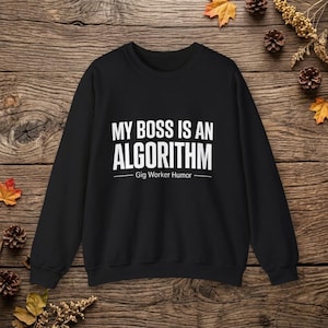 May include: A black long-sleeve sweatshirt featuring white text that reads MY BOSS IS AN ALGORITHM with the subtext Gig Worker Humor centered below the main phrase. The garment has a crew neckline, long sleeves, and ribbed cuffs and hem.
