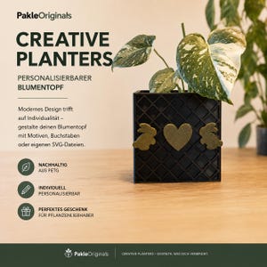 Könnte beinhalten: Ein quadratischer schwarzer Blumentopf mit Gittermuster, verziert mit zwei goldenen Hasensilhouetten und einem goldenen Herz in der Mitte. Der Topf enthält eine grün-weiß panaschierte Pflanze. Der Text lautet PakleOriginals CREATIVE PLANTERS.