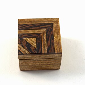 May include: A small wooden box with a geometric pattern on the lid. The box is made of dark wood with light brown accents.