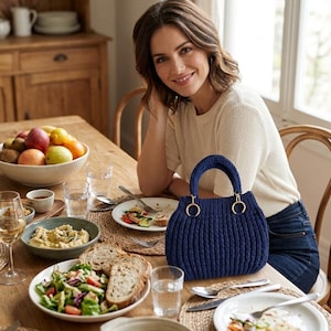 May include: A dark blue handbag with a ribbed knit texture, featuring two rounded handles attached to the bag with gold-toned metal rings. The bag has a structured, curved silhouette and is crafted from a thick, durable yarn material.