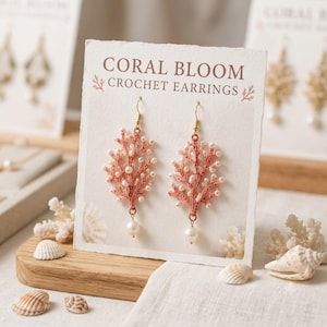 May include: A pair of coral-colored crochet earrings shaped like branching coral, accented with small white beads and a single dangling pearl at the base. The earrings are displayed on a white card labeled CORAL BLOOM CROCHET EARRINGS.