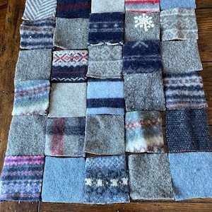 May include: A patchwork of various wool fabric squares in shades of gray, blue, and red. Each square features unique patterns, including stripes, snowflakes, and geometric designs. The arrangement creates a textured, handcrafted appearance.