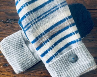 May include: A pair of knitted mittens with a striped pattern in blue, white, and tan. The cuffs are gray and feature a button detail. The mittens are designed for warmth and comfort, perfect for cold weather.