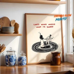 Puede incluir: Una lámina artística enmarcada con fondo crema y un dibujo lineal negro de dos figuras bailando sobre un disco de vinilo. El texto "LOVE'S NEVER WASTED WHEN ITS SHARED" aparece en letras rojas. La lámina está dentro de un marco de madera.