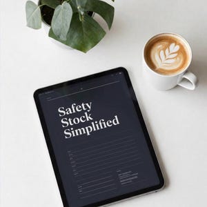 以下が含まれることがあります： ダークグレーの背景に白い文字で「Safety Stock Simplified」と表示されたタブレット。画面にはデータ入力用の線が並んでおり、在庫管理用の構造化されたレイアウトが示されています。横には白いコーヒーカップが置かれています。