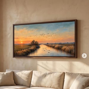 Peut inclure: Une peinture de paysage rectangulaire dans un cadre brun foncé représentant un coucher de soleil sur une rivière calme. La scène montre une lumière dorée se reflétant sur l'eau, des herbes hautes sur les rives et un vol d'oiseaux dans le ciel orange.