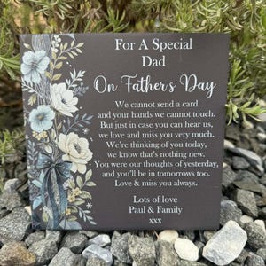 Pode incluir: Uma placa quadrada de ardósia com acabamento cinza escuro, apresentando uma ilustração floral branca no lado esquerdo e texto branco que diz: For A Special Dad On Father's Day, seguido de um poema memorial e assinado: Lots of love Paul & Family XXX.