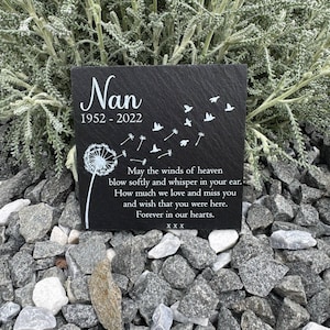 Puede incluir: Una placa conmemorativa cuadrada de pizarra negra con grabado blanco que dice Nan 1952-2022, un diseño de diente de león con semillas que se convierten en pájaros y el poema May the winds of heaven blow softly and whisper in your ear. Forever in our hearts. xxx